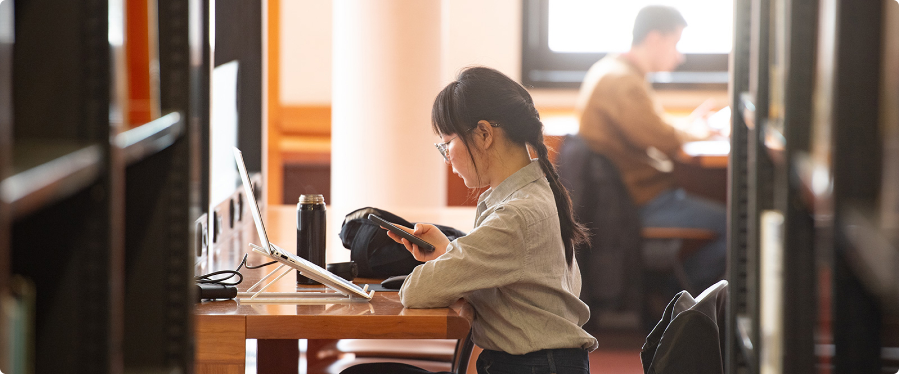 A student sat in a library, looking at their phone